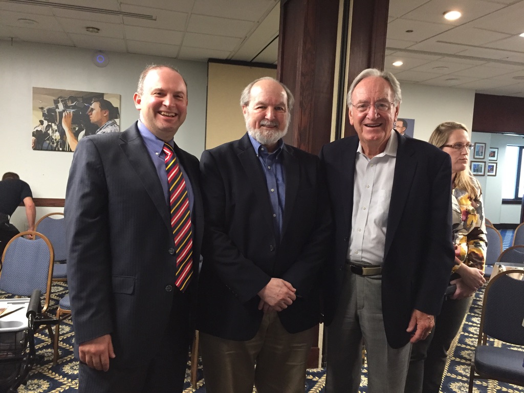 Three men in dark suits smiling for the camera