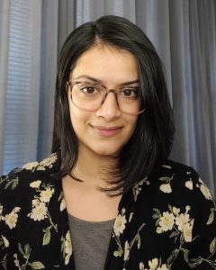 A headshot of a woman with dark hair and glasses